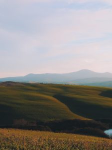 Idyllic landscape of rolling hills in Tuscany at sunrise, featuring lush green fields and distant mountains.